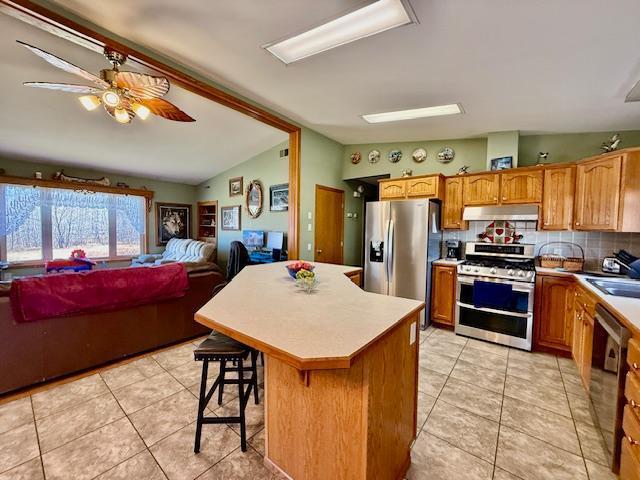 kitchen featuring a ceiling fan, stainless steel appliances, vaulted ceiling, light countertops, and under cabinet range hood