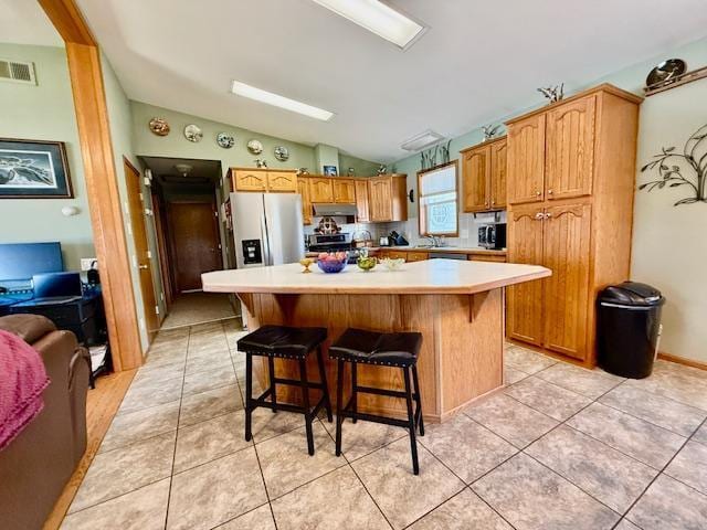 kitchen with visible vents, light tile patterned flooring, light countertops, vaulted ceiling, and appliances with stainless steel finishes