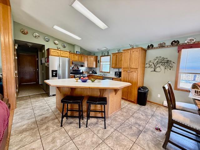 kitchen featuring a kitchen island, lofted ceiling, light tile patterned flooring, stainless steel appliances, and light countertops