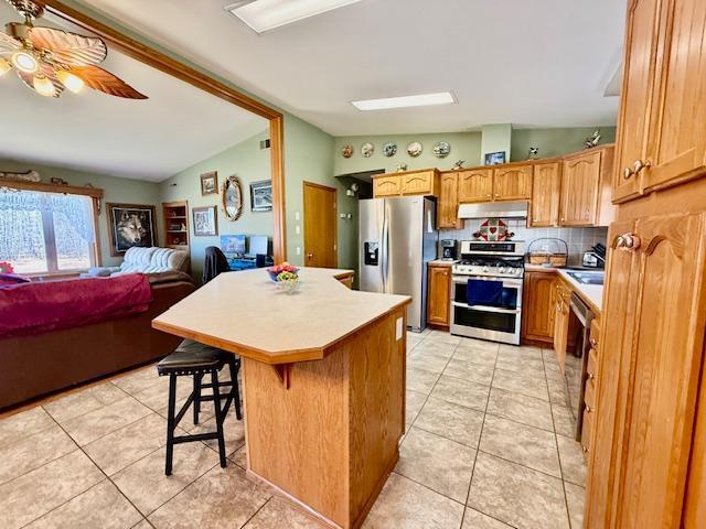 kitchen featuring light tile patterned floors, light countertops, vaulted ceiling, under cabinet range hood, and appliances with stainless steel finishes