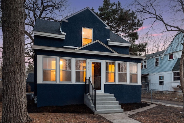 view of front of house with stucco siding, entry steps, a shingled roof, and fence