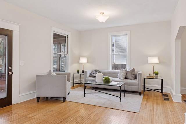 living room featuring light wood-style flooring, plenty of natural light, visible vents, and baseboards