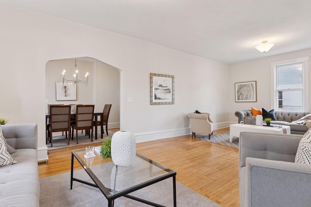 living area with an inviting chandelier, wood finished floors, arched walkways, and baseboards