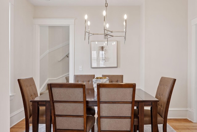 dining space with baseboards, stairs, an inviting chandelier, and wood finished floors