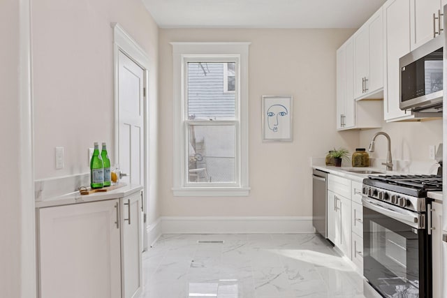 kitchen featuring marble finish floor, a sink, white cabinetry, appliances with stainless steel finishes, and baseboards