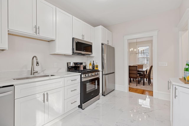 kitchen featuring marble finish floor, a sink, white cabinetry, appliances with stainless steel finishes, and an inviting chandelier