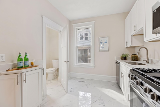 kitchen featuring baseboards, light countertops, appliances with stainless steel finishes, marble finish floor, and a sink