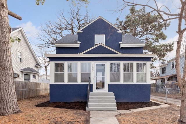 view of front of property with stucco siding, entry steps, roof with shingles, and fence