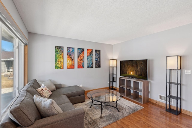 living area featuring visible vents, wood finished floors, baseboards, and a textured ceiling