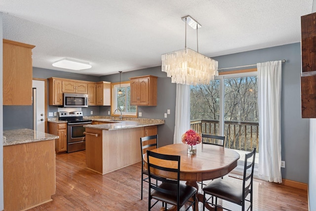 kitchen featuring a peninsula, a notable chandelier, light wood-type flooring, and appliances with stainless steel finishes