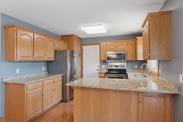 kitchen featuring light stone counters, a peninsula, light wood-style floors, stainless steel appliances, and a sink