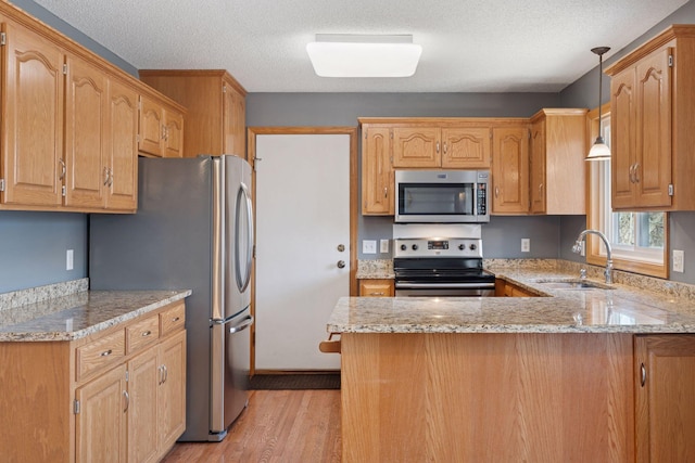 kitchen with light stone countertops, light wood finished floors, a peninsula, a sink, and stainless steel appliances