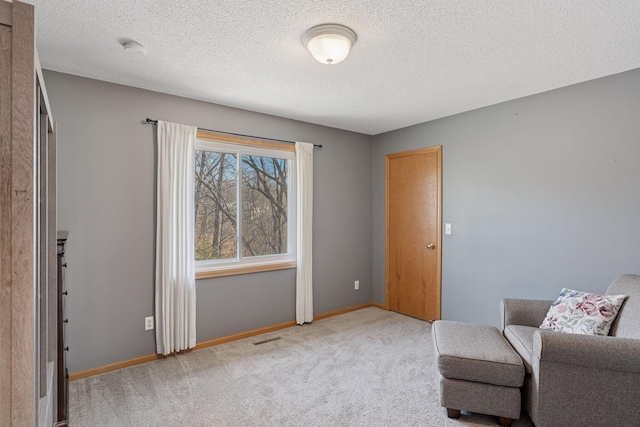 sitting room with a textured ceiling, baseboards, and carpet