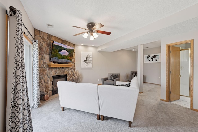 living room with visible vents, a ceiling fan, a textured ceiling, a stone fireplace, and light colored carpet