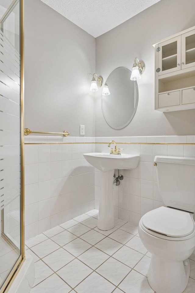 bathroom featuring a textured ceiling, wainscoting, tile patterned floors, toilet, and a shower with door