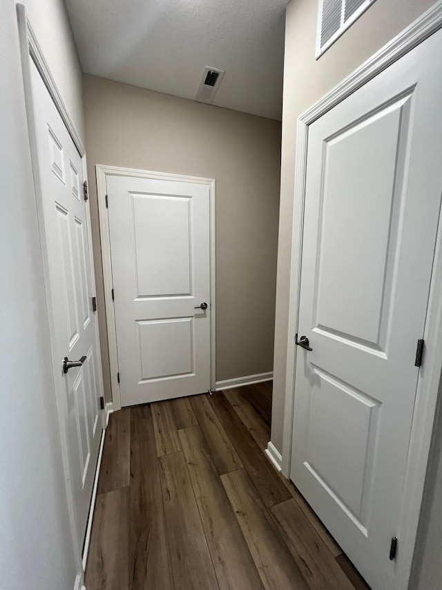 hall featuring visible vents, baseboards, and dark wood-style flooring