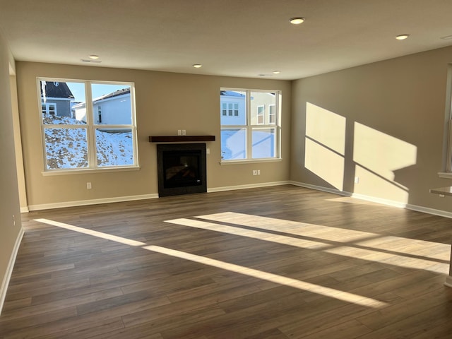 unfurnished living room with a glass covered fireplace, recessed lighting, dark wood-type flooring, and baseboards