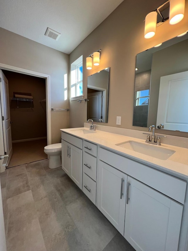 bathroom with double vanity, visible vents, toilet, and a sink