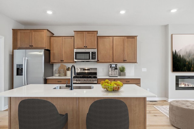 kitchen featuring tasteful backsplash, light countertops, appliances with stainless steel finishes, light wood-style floors, and a sink