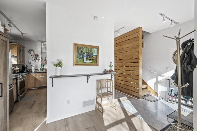 kitchen with stainless steel range with gas stovetop, dark countertops, dark wood-style floors, visible vents, and track lighting