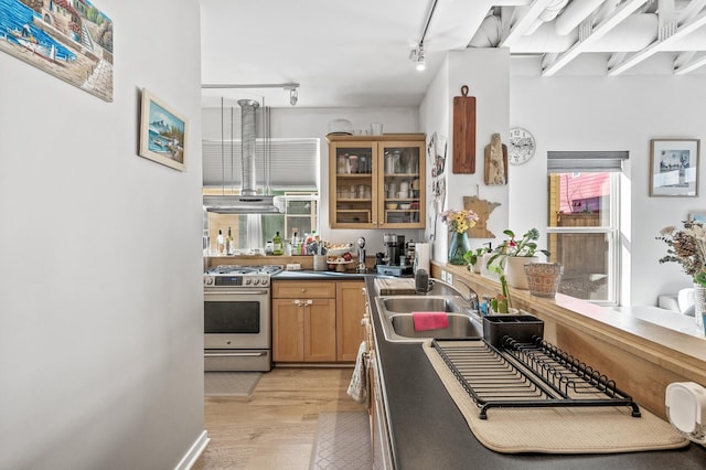 kitchen featuring light wood-type flooring, a sink, stainless steel gas range, extractor fan, and brown cabinetry
