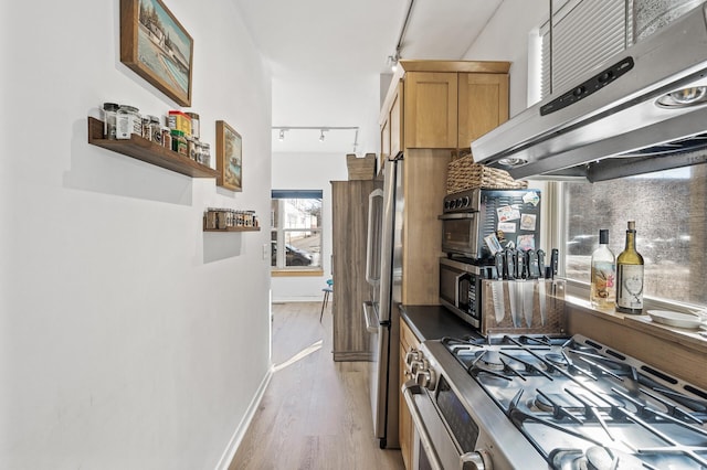 kitchen with light wood-style flooring, track lighting, baseboards, stainless steel appliances, and extractor fan