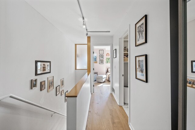corridor with rail lighting, an upstairs landing, and light wood-style floors