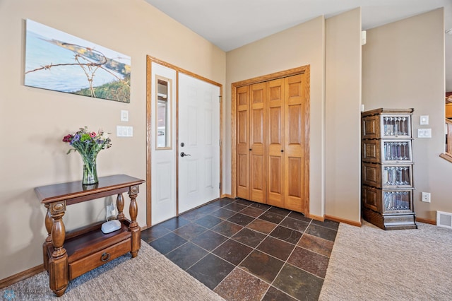 foyer entrance with visible vents, baseboards, and dark carpet