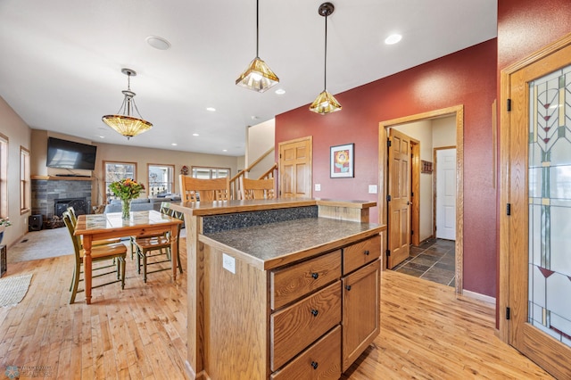 kitchen featuring light wood-style flooring, a fireplace, recessed lighting, dark countertops, and decorative light fixtures