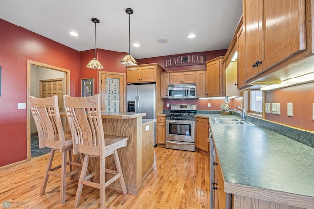 kitchen featuring light wood finished floors, a kitchen island, appliances with stainless steel finishes, and a sink