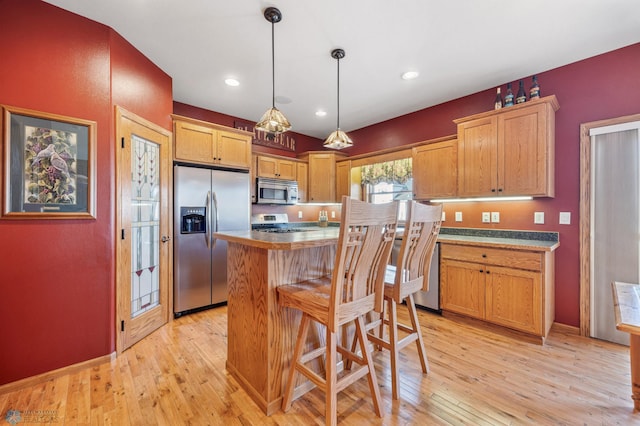 kitchen with light wood finished floors, hanging light fixtures, appliances with stainless steel finishes, a kitchen breakfast bar, and a center island