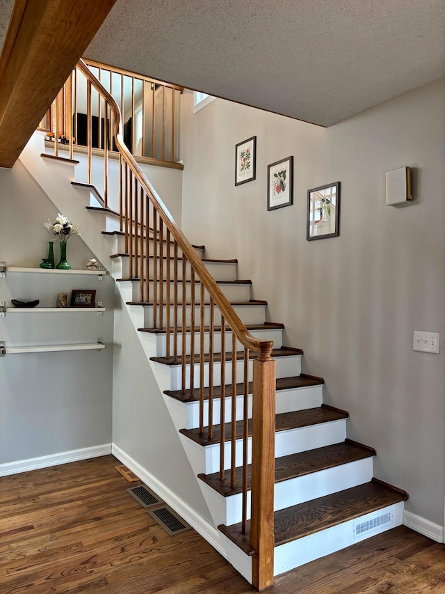 stairs with visible vents, wood finished floors, baseboards, and a textured ceiling