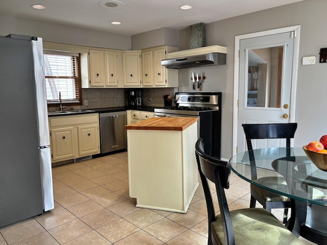 kitchen featuring light tile patterned floors, stainless steel appliances, wood counters, cream cabinets, and backsplash