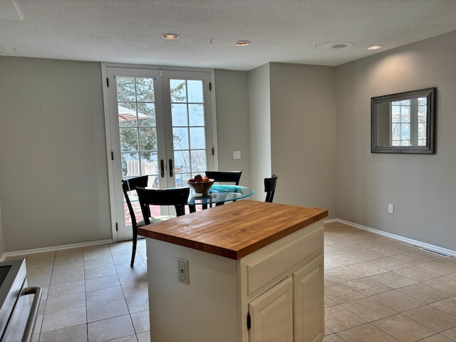 kitchen featuring a textured ceiling, french doors, butcher block counters, light tile patterned floors, and baseboards