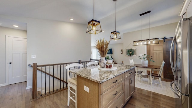 kitchen with a center island, a breakfast bar area, a barn door, freestanding refrigerator, and dark wood-style flooring