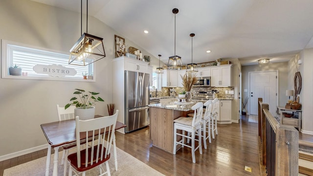 kitchen featuring backsplash, a kitchen island, white cabinetry, stainless steel appliances, and vaulted ceiling