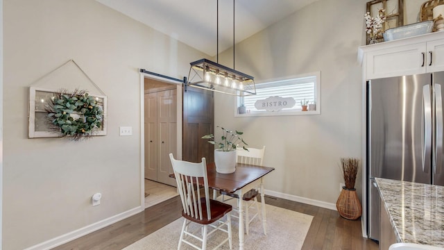 dining room with a barn door, baseboards, dark wood-style flooring, and vaulted ceiling