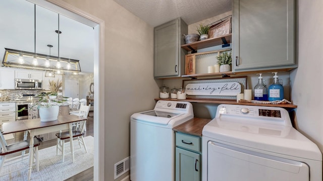 laundry area featuring a textured ceiling, cabinet space, visible vents, and washing machine and clothes dryer