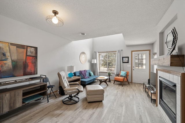 living area featuring a tiled fireplace, a textured ceiling, light wood-style floors, and vaulted ceiling