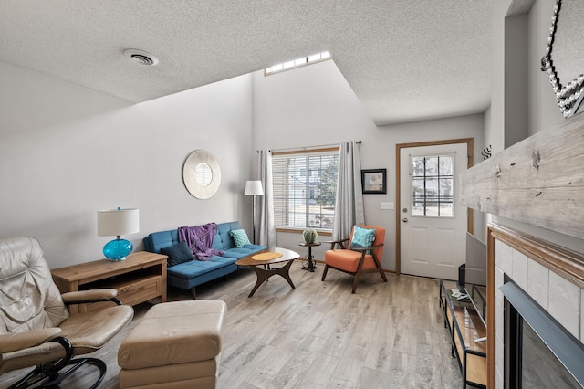 living room featuring visible vents, a textured ceiling, a fireplace, and light wood finished floors