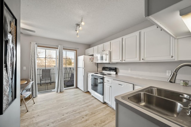 kitchen with light wood finished floors, a textured ceiling, white appliances, white cabinetry, and a sink