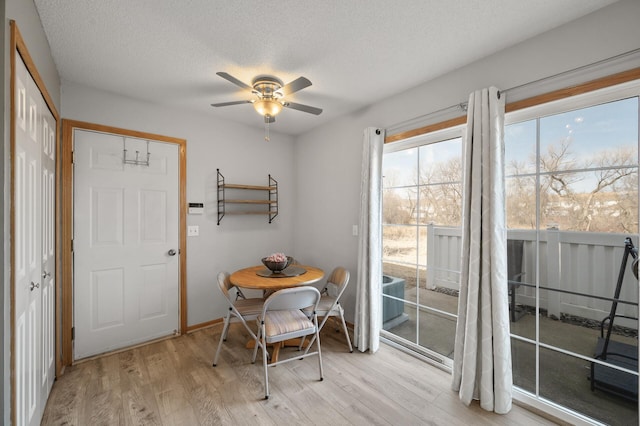 dining space featuring light wood-type flooring, baseboards, a textured ceiling, and ceiling fan