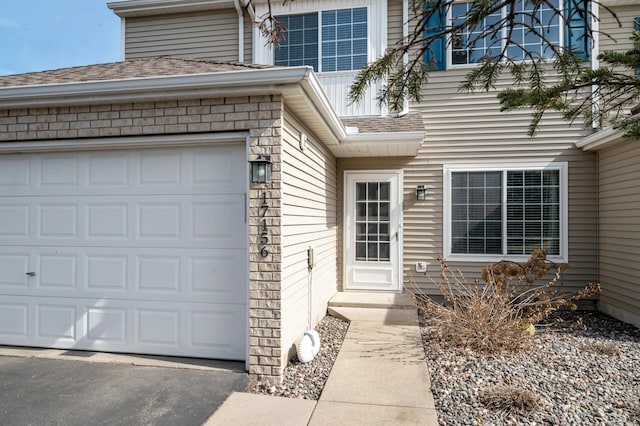 doorway to property featuring an attached garage, driveway, and roof with shingles