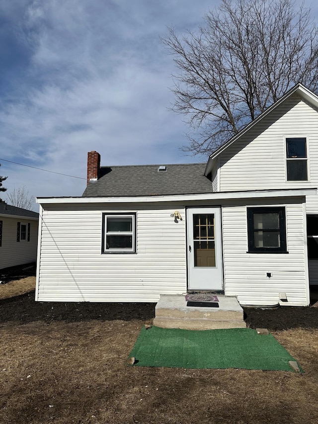 back of house with a chimney and roof with shingles