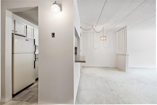 hall with a textured ceiling, carpet flooring, wood finished floors, and a chandelier