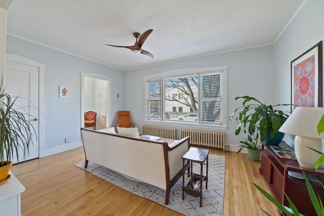 living room featuring light wood finished floors, radiator heating unit, ceiling fan, a textured ceiling, and crown molding