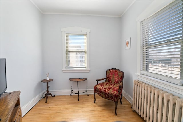 sitting room featuring light wood-style flooring, radiator heating unit, baseboards, and ornamental molding