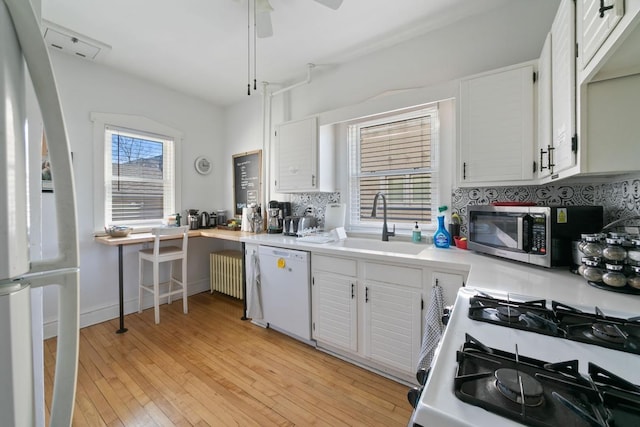 kitchen with a sink, white appliances, radiator, light countertops, and decorative backsplash