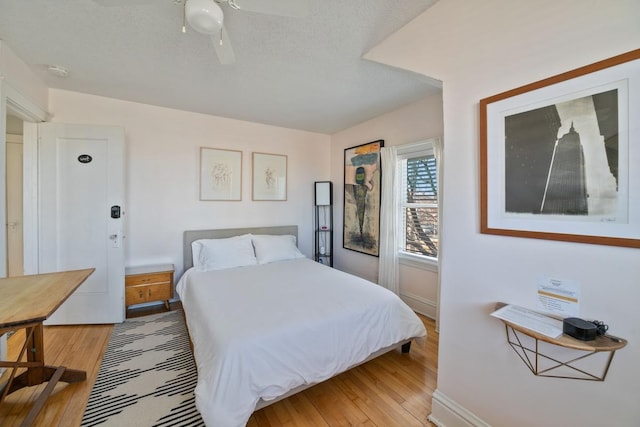 bedroom with light wood-style flooring, a textured ceiling, baseboards, and ceiling fan