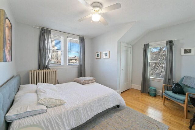 bedroom with multiple windows, light wood-style flooring, radiator heating unit, and baseboards